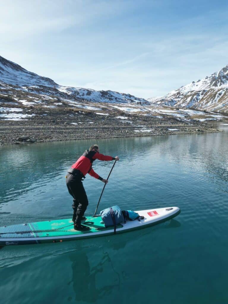 Opti paddleboard avec pagaie en eaux calmes montagnes enneigées en arrière-plan.