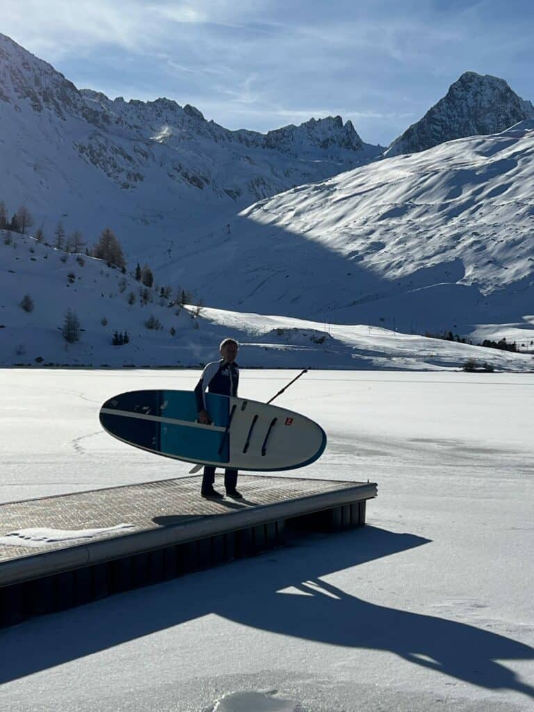 Pratique du paddle sur neige dans un paysage montagnard enneigé.