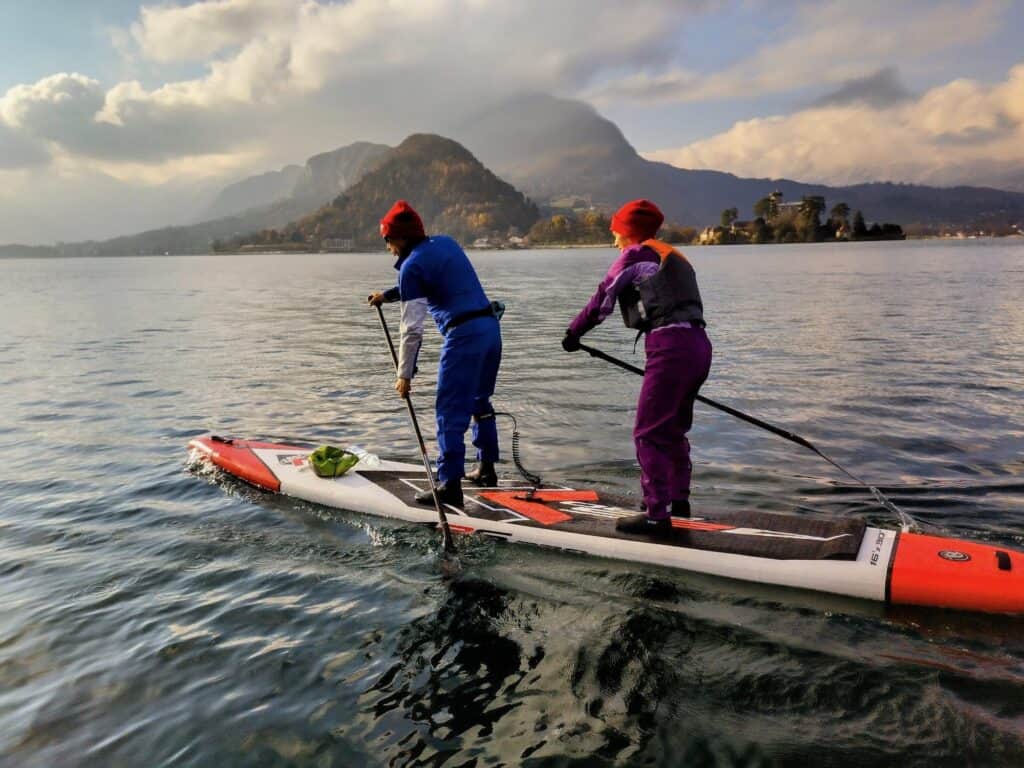 Pratique du paddle opti avec deux personnes sur une planche stable en lac naturel.