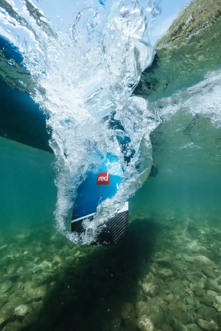 Pagaie Red Paddle Co Prime Carbone plongeant dans l'eau avec explosion de bulles — guide choisir sa pagaie SUP