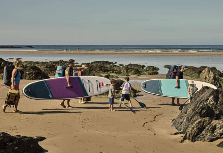 Famille marchant vers l’eau avec ses paddles gonflables Red Paddle, l’été